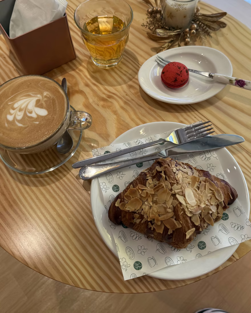 盘中的杏仁可颂,旁边是一杯拿铁和一颗红色马卡龙