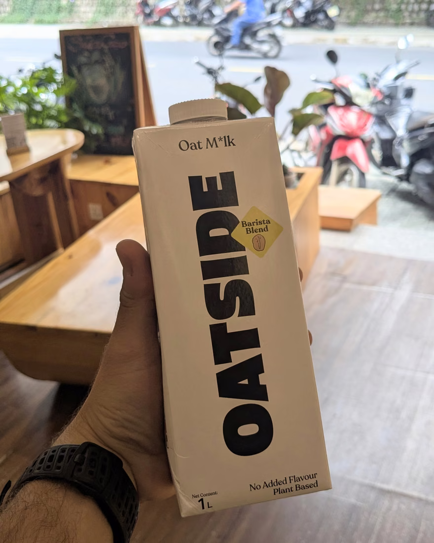 手里拿着一盒 Oatside 燕麦奶,后方是店内空间